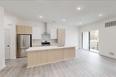 Located at 137 Texas Road in Marlboro Township, NJ, this contemporary multi-floor home offers a well-organized layout across three levels. The ground floor features an attached garage with an automatic opener, providing secure parking and additional storage space alongside a finished flex room with recessed lighting and light wood-tone flooring. The main living level centers on an open-concept kitchen and living area. The kitchen is appointed with sleek, light wood cabinetry, stainless steel appliances including a gas range and French door refrigerator, a white quartz waterfall island with an undermount sink, and recessed lighting throughout. Light luxury vinyl plank flooring flows seamlessly across all levels, lending a cohesive, modern aesthetic. The upper floor houses two bedrooms, including a generously sized primary bedroom with recessed lighting and a large window framing wooded outdoor views. The second bedroom also benefits from natural light and serene tree-lined views. Three well-appointed bathrooms feature modern vanities with warm wood cabinetry, framed mirrors, and clean white finishes. A dedicated laundry area with a full-size washer and dryer adds everyday convenience. Crisp white walls, natural wood stair railings with white balusters, and abundant natural light define the home's clean, minimalist character throughout.