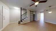 This two-story home in New Braunfels, Texas offers a thoughtfully designed layout with contemporary finishes throughout. The main living area features light luxury vinyl plank flooring, ceiling fans, and a striking staircase with dark wood treads and black metal balusters. A standout rustic sliding barn door with frosted glass panels adds character and serves as a functional design element connecting spaces on the main floor. The kitchen is well-appointed with gray shaker-style cabinetry, stainless steel appliances including a range, refrigerator, and dishwasher, complemented by a decorative patterned tile backsplash and light quartz countertops. A sliding glass door in the kitchen brings in natural light and provides outdoor access. Upstairs, the bedrooms feature plush carpeting, ceiling fans, and windows with blinds that allow for natural light. The bathrooms are finished with clean, modern details including undermount sinks, matte black fixtures, large mirrors, and a tiled tub-and-shower combination featuring a decorative mosaic accent border. Throughout the home, neutral tones and consistent design choices create a cohesive, move-in-ready atmosphere well suited for comfortable living.