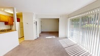 This single-floor unit is designed with a practical, open layout that connects the living and dining areas seamlessly. The main living space is generously sized, finished with wall-to-wall neutral carpeting and crisp white walls that create a clean, bright atmosphere. A large sliding glass door fitted with vertical blinds spans one wall, allowing natural light to pour in and offering a view of greenery outside. The open passage between the living and adjoining room enhances the sense of spaciousness and flow throughout the unit.

The kitchen is positioned adjacent to the main living area and features warm honey-toned oak cabinetry with ample upper and lower storage. Light granite-style countertops complement the stainless steel sink, while white appliances including a range with overhead ventilation complete the functional workspace. The kitchen is finished with neutral tile flooring, providing a practical transition from the carpeted living areas.

The bathroom includes a full tub-and-shower combination with white subway tile surround and chrome fixtures, conveying a clean and classic aesthetic. A built-in closet with shelving is also present, adding convenient storage options. Throughout the unit, large windows ensure consistent natural light, contributing to an overall bright and airy ambiance.