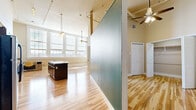 This single-floor unit offers a well-designed layout that maximizes its efficient footprint through thoughtful architectural details. The open living area is defined by notably high ceilings that lend a sense of spaciousness well beyond what the floor area alone might suggest. A distinctive translucent glass partition divides the space while maintaining visual openness and allowing natural light to flow freely throughout. Large, multi-pane windows line one wall of the main living area, bathing the hardwood floors in abundant natural light and providing outward views. Ceiling fans are installed in both the living area and an adjacent zone, contributing to air circulation throughout.

The kitchen is efficiently arranged with dark espresso cabinetry, granite countertops with a tile backsplash, and a full suite of stainless steel appliances including a refrigerator, electric range, over-range microwave, and dishwasher. A kitchen island with a matching granite surface provides additional workspace.

The bathroom continues the consistent design language with dark cabinetry, granite countertop vanity, an overhead storage cabinet, and the same light hardwood flooring found throughout the unit. A dedicated closet features built-in shelving and a hanging rod, offering organized storage space.