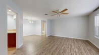 Located at 5511 Executive Dr in New Port Richey, Florida, this single-story, 2-bedroom, 2-bathroom home offers a well-designed layout with a comfortable, functional flow. Light wood-look flooring runs throughout the living areas and bedrooms, complemented by soft neutral gray walls and white baseboards that create a clean, cohesive aesthetic. Textured ceilings and ceiling fans are present in every room, adding both character and practicality in the Florida climate. The open living and dining area is highlighted by an elegant chandelier and connects seamlessly to the kitchen via a pass-through window with a breakfast bar, where warm wood cabinetry and white appliances are visible. A sliding glass door in one room provides direct outdoor access and fills the space with natural light and greenery views. The primary bedroom is generously sized, featuring a charming bay window that invites abundant natural light. The second bedroom also benefits from a window with outdoor views and its own ceiling fan. Both bathrooms include warm wood-toned vanities with single-sink countertops and large mirrors. The primary bath offers a walk-in tiled shower, while the second bath features a tub-shower combination. Two closets provide ample storage throughout the home.
