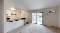 Located in Huntington Beach, California, this one-bedroom, two-bathroom residence offers a well-organized single-floor layout designed to maximize functionality. The living room features vaulted ceilings that add a sense of openness, soft carpeting underfoot, and a full-width sliding glass door dressed with vertical blinds that allows natural light to pour in while providing direct access to an outdoor area with views of surrounding greenery.

The kitchen is efficiently designed with a pass-through counter that opens to the living room, creating a connected feel. It is outfitted with white cabinetry, dark granite-style countertops, stainless steel appliances including an electric range and over-the-range microwave, and wood-look flooring that adds warmth to the space.

The bedroom is a comfortable, carpeted retreat with clean white walls and ample room for furnishings. Two bathrooms serve the unit — one featuring a wide vanity with dark granite-style countertops, white cabinetry, and a large mirror with overhead lighting, and the other a full bath with a shower/tub combination and wood-look flooring. A hallway connects the rooms, contributing to a practical and cohesive flow throughout the home.