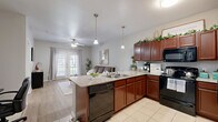 This thoughtfully designed one-bedroom, one-bathroom residence offers a cohesive, single-floor layout that maximizes both function and comfort. The open-concept kitchen and living area serves as the heart of the home, where rich mahogany cabinetry, granite countertops, and black appliances define the kitchen space. A peninsula with bar seating and pendant lighting above creates a natural gathering spot and seamlessly connects to the living area. Light wood-style flooring runs throughout the main living spaces, complementing the neutral gray tones on the walls. The living room features a ceiling fan and French doors that invite ample natural light and provide outdoor access. The bedroom is a comfortable retreat, featuring wood-style flooring, dual windows for natural light, and a ceiling fan. A dedicated closet offers convenient storage. The hallway connects the main living areas to the private spaces, including the full bathroom, which features tile flooring, a dark wood vanity with a dark stone countertop, and a framed mirror. The overall ambiance of the residence is clean, modern, and inviting, with consistent finishes tying each space together cohesively.