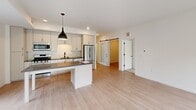 Located at 393 Marshall Ave in Saint Paul, Minnesota, this single-floor unit showcases a contemporary design defined by clean lines, a neutral palette, and an abundance of natural light. The open-concept living and kitchen area serves as the heart of the space, where light wood laminate flooring extends seamlessly throughout. The kitchen is well-appointed with white shaker-style cabinetry reaching toward the ceiling, dark countertops, stainless steel appliances including a gas range, built-in microwave, and French door refrigerator, and a central island with pendant lighting above. A sliding glass door connects the living area to a private balcony, offering views of the surrounding neighborhood's mature tree canopy.

The living space benefits from oversized black-framed windows that flood the interior with natural light and frame outdoor views. A sliding barn door adds a stylish architectural detail separating the living area from the private quarters. Bedrooms feature plush carpeting, generous black-framed windows, and ample closet space. At least one bedroom connects directly to a bathroom. The bathrooms feature white vanity cabinetry, large mirrors, and a tub-shower combination, maintaining the unit's clean, modern aesthetic throughout.