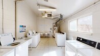 Located at 11501 Dorchester St in Southgate, Michigan, this shared laundry facility is a single-floor space designed to serve the practical needs of its users. The room is constructed with painted concrete block walls and features light-colored tile flooring throughout, giving it a clean and utilitarian appearance.

The facility is well-equipped with multiple top-load washing machines and dryers arranged along both sides of the room, maximizing the available floor space. Utility sinks are also present, providing additional functionality for hand-washing or other laundry tasks. A folding table with chairs is positioned centrally, offering a convenient spot for residents to sort and fold laundry while waiting.

Overhead, fluorescent lighting ensures the space is well-lit, supplemented by natural light from windows on the side and rear walls. A ceiling-mounted HVAC unit and visible ductwork keep the environment comfortable year-round. A water heater with copper piping is also housed within the space. A door at the rear of the room provides direct access to the exterior. Informational signage on the walls offers guidance on proper use of the top-load washers and dryers. Overall, the facility is straightforward and functional, providing essential laundry amenities in a compact, organized layout.