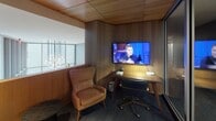 Located at 900 7th St SW in Washington, DC, this thoughtfully designed single-floor space blends contemporary style with functional comfort. The interior is defined by rich warm wood paneling and ceilings that lend a refined, inviting atmosphere throughout.

A standout feature is the floor-to-ceiling built-in bookcase set against a deep navy blue accent wall, filled with books and decorative objects, and paired with a mustard yellow lounge chair — creating a cozy reading nook that balances aesthetics with utility. The flooring throughout transitions between sleek tile in the elevator lobby and soft, textured carpet in the lounge and work areas.

The space includes a private workstation nook enclosed by wood-paneled walls, equipped with a wall-mounted flat-screen television, a desk with task lighting, and a leather accent chair — ideal for focused individual work or media viewing. Glass partitions and doors allow sightlines across zones while maintaining a sense of separation between areas.

A polished elevator lobby with stainless steel doors and modern digital displays adds a professional, high-end touch. Recessed lighting throughout enhances the warm tones of the wood finishes, while an ornamental pendant light fixture adds an artistic focal point. The overall ambiance is one of quiet sophistication, combining lounge comfort with functional workspaces in a cohesive, modern design.