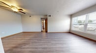 This single-floor unit offers a practical and well-designed layout with a clean, neutral aesthetic throughout. The open living area is spacious and bright, featuring durable luxury vinyl plank flooring in a warm gray tone, wood baseboards, and a textured ceiling with a ceiling fan overhead. A pass-through counter connects the living space to the kitchen, which is equipped with gray shaker-style cabinetry, granite-look countertops, and stainless steel appliances including a full-size refrigerator.

The bedrooms are carpeted for comfort, with one room offering a generously sized walk-in closet and a window allowing natural light and outdoor views. An additional room features plush carpet and ample wall space. The bathroom is neatly appointed with a shaker-style vanity, white countertop, large mirror, overhead lighting, and wood-look LVP flooring. A dedicated laundry area accommodates a full-size top-load washer, with hookups available for a dryer as well.

A hallway connects the main living areas to the private rooms, framed by warm wood-toned doors. Throughout, the unit maintains a consistent palette of soft whites and grays, creating a cohesive and move-in-ready environment.