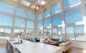 This 890 square foot solarium apartment in Seattle offers a striking blend of modern design and breathtaking views. The heart of the space is an expansive open-concept living area, defined by its soaring ceiling and wall-to-wall, floor-to-ceiling windows that flood the interior with natural light. These windows frame panoramic vistas of the city skyline and nearby water, creating a seamless connection between indoor and outdoor environments.

The living area is thoughtfully furnished with contemporary pieces, including a plush sectional sofa, uniquely designed blue armchairs, and a statement coffee table with a live-edge wood design. A long, sleek desk area spans one wall, ideal for work or creative pursuits.

The kitchen, while compact, is efficiently designed with modern appliances and ample counter space. The bathroom continues the contemporary aesthetic with a minimalist design, featuring hexagonal tile accents and wood-look flooring.

Throughout the apartment, a cohesive color palette of blues, whites, and natural wood tones creates a calming atmosphere that complements the expansive views. The hardwood floors add warmth and tie the space together.

This solarium apartment, located at 1275 Mercer St in Seattle, exemplifies urban living at its finest, offering a perfect balance of style, function, and spectacular views in an enviable location.
