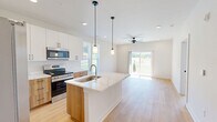 Located at 2636 Toccoa Byp in Toccoa, Georgia, this thoughtfully designed single-story home offers two bedrooms and two bathrooms within a well-utilized floor plan. Light hardwood flooring flows consistently throughout the home, creating a warm and cohesive aesthetic against the clean white walls and modern trim.

The kitchen is a standout feature, showcasing a two-tone design with white upper cabinetry and warm wood-grain lower cabinets, all topped with striking white quartz countertops with subtle veining. A central island with an integrated sink provides additional prep space, while stainless steel appliances, including a French door refrigerator, electric range, and built-in microwave, complete the functional layout. Pendant lighting over the island adds a contemporary touch.

The primary bedroom is generously sized with a ceiling fan and direct access to an en-suite bathroom featuring a wood-tone vanity and dedicated toilet and shower area. The second bedroom is bright and well-proportioned, benefiting from dual windows that invite natural light and outdoor views. A full hallway bathroom includes a tub-shower combination with white subway tile and a matching wood-tone vanity. The home also features an outdoor deck area, extending the living space to the exterior.