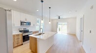 Located at 2636 Toccoa Byp in Toccoa, Georgia, this thoughtfully designed single-story home offers two bedrooms and two bathrooms within a well-utilized floor plan. Light hardwood flooring flows consistently throughout the home, creating a warm and cohesive aesthetic against the clean white walls and modern trim.

The kitchen is a standout feature, showcasing a two-tone design with white upper cabinetry and warm wood-grain lower cabinets, all topped with striking white quartz countertops with subtle veining. A central island with an integrated sink provides additional prep space, while stainless steel appliances, including a French door refrigerator, electric range, and built-in microwave, complete the functional layout. Pendant lighting over the island adds a contemporary touch.

The primary bedroom is generously sized with a ceiling fan and direct access to an en-suite bathroom featuring a wood-tone vanity and dedicated toilet and shower area. The second bedroom is bright and well-proportioned, benefiting from dual windows that invite natural light and outdoor views. A full hallway bathroom includes a tub-shower combination with white subway tile and a matching wood-tone vanity. The home also features an outdoor deck area, extending the living space to the exterior.