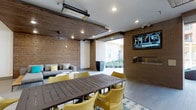 This indoor/outdoor living area is thoughtfully designed to blur the boundary between interior comfort and open-air enjoyment. The space features a striking combination of warm wood-paneled ceilings and exposed brick accent walls, creating a welcoming, lodge-inspired atmosphere. Overhead, ceiling-mounted infrared heaters and recessed lighting ensure year-round usability, while a ceiling fan adds additional climate control.

A large, dark-stained wood dining table surrounded by bold yellow woven chairs serves as the central gathering point, anchored by a patterned area rug. Along one wall, a built-in fireplace adds ambiance and warmth, positioned beneath a wall-mounted flat-screen television—ideal for entertaining. A comfortable upholstered lounge sofa with gray and yellow accent pillows offers a more relaxed seating option nearby.

A wide, retractable opening connects the covered area directly to an exterior courtyard, flooding the space with natural light and providing seamless flow between indoors and outdoors. The overall design balances functionality with a modern, inviting aesthetic suited for both casual gatherings and social events.