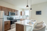 Located at 108 S Bristol St in Sun Prairie, WI, this thoughtfully designed one-bedroom, one-bathroom unit offers a clean, modern aesthetic throughout its single-floor layout. Light hardwood flooring flows continuously across every room, tying the space together with a warm, cohesive feel.

The welcoming entrance leads into an open-concept living area bathed in natural light. The living room features a wall-mounted mini-split system for year-round comfort, complemented by stylish flush-mount lighting and a neutral color palette that enhances the sense of openness.

The kitchen is a standout feature, equipped with warm wood cabinetry, white quartz countertops, a subway tile backsplash, and stainless steel appliances including a range, microwave, and dishwasher. A central island with seating for two, illuminated by sleek pendant lights, serves as both a prep space and casual dining area. Large windows offer pleasant outdoor views.

The dedicated dining area accommodates a full-sized table and benefits from expansive windows that flood the space with natural light and provide views of the surroundings.

The bedroom is quiet and comfortably scaled, while the bathroom features a warm wood vanity with dark countertop, a backlit mirror, and a glass-door walk-in shower with matte black hardware — a polished, spa-like finish.