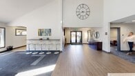 Located at 2201 104th St S in Tacoma, Washington, this single-story community clubhouse for Altitude 104 offers a well-appointed, multi-functional space designed for both resident services and recreation. The interior is defined by soaring vaulted ceilings, an abundance of natural light from strategically placed skylights, and wood-look tile flooring that flows throughout the main areas.

Upon entry, a welcoming reception area serves as the leasing office, featuring a branded Altitude 104 accent wall, carpeted work zone, and an open layout that allows staff to interact easily with visitors. Adjacent to the entry is a versatile lounge area with bar-height seating, a large wall clock, and colorful artwork, transitioning into a relaxed gathering space anchored by a reclaimed wood accent wall, a tile-surround fireplace, a wall-mounted television, and comfortable leather seating beneath a bank of skylights.

The game room is equipped with a pool table and shuffleboard, with direct access to an outdoor pool area through large glass doors and windows. A fully equipped kitchen with stainless steel appliances, two-tone cabinetry, and a tile backsplash supports events and daily resident use. A dedicated fitness center rounds out the amenities, featuring treadmills, cable equipment, floor-to-ceiling mirrors, mounted televisions, and vibrant multi-colored flooring.