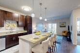 This thoughtfully designed 1-bedroom, 1-bathroom residence offers a comfortable and modern living experience across a single floor. The open-concept kitchen and living area serves as the heart of the home, where rich dark-walnut cabinetry, light countertops, and a full suite of stainless steel appliances—including a refrigerator, range, and built-in microwave—create a sleek, functional kitchen. A central island with bar seating and stylish pendant lighting above makes the space ideal for both casual dining and entertaining. Hardwood-style flooring extends throughout the main living area, complementing the bright, neutral palette. The living room is generously sized, featuring a sliding glass door that opens to a private balcony, filling the space with natural light and offering pleasant outdoor views. The bedroom is a serene retreat, finished with plush carpeting, a large window with scenic views, a ceiling fan, and direct access to a dedicated walk-in closet with built-in shelving. The full bathroom features rich wood cabinetry with brushed nickel hardware, a wide vanity with an oversized mirror, and a full tub-shower combination. Clean lines and a cohesive modern design aesthetic tie all rooms together seamlessly.