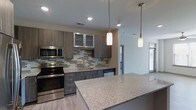 Located at 200 E Six Forks Rd in Raleigh, North Carolina, this single-floor space offers a contemporary and well-appointed interior designed for both comfort and functionality. The open-concept layout connects the kitchen seamlessly to the living area, creating an airy and cohesive flow throughout the unit. The kitchen is a standout feature, showcasing dark wood-toned cabinetry with frosted glass upper cabinet inserts, a decorative mosaic tile backsplash in neutral earth tones, and a generous granite-topped island that provides ample prep and dining space. Stainless steel appliances — including a range, microwave, and dishwasher — complement the modern aesthetic. Pendant lighting fixtures hang above the island, adding warmth and a stylish focal point to the kitchen. Light wood-look flooring extends throughout, contributing to the bright and clean atmosphere. Recessed lighting in the ceiling ensures consistent illumination across the space. The adjacent living area benefits from natural light streaming through large windows with blinds, enhancing the open and welcoming character of the interior. The overall design reflects a modern, move-in-ready aesthetic with quality finishes throughout.