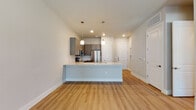 This thoughtfully designed single-floor residence showcases a contemporary open-concept layout that seamlessly connects the kitchen and living areas. The kitchen is a standout feature, equipped with stainless steel appliances including a refrigerator, electric range, and over-the-range microwave. Gray shaker-style cabinetry with sleek hardware lines the walls, complemented by a white subway tile backsplash and light quartz countertops. A spacious kitchen island with a built-in sink and matching quartz surface doubles as a breakfast bar, anchored by pendant lighting overhead. Warm wood-look flooring flows throughout the main living areas, adding continuity and a natural aesthetic. The living area offers generous proportions with a ceiling fan and a neutral color palette that enhances the bright, airy ambiance. The bedroom features a ceiling fan, a window with outdoor views of mature trees, and direct access to a well-appointed bathroom. The bathroom is finished with large-format tile flooring, a gray double vanity with granite countertops, a soaking tub, and marble-style tile walls in the shower. Recessed lighting throughout ensures a clean, modern look across the entire space.