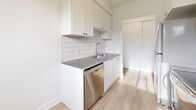 This well-appointed one-bedroom, one-bathroom unit at 9 Amos Ave, Unit 7 offers a thoughtfully designed single-floor layout with a clean, modern aesthetic throughout. Light wood-style flooring runs continuously across the living, dining, and bedroom areas, complementing the crisp white walls and trim that give the space a bright, airy feel.

The combined kitchen and dining area serves as the functional heart of the unit. The kitchen features white shaker-style cabinetry extending to the upper walls, grey countertops, a white subway tile backsplash, and stainless steel appliances including a full-size refrigerator and dishwasher. A window in the dining area overlooks surrounding greenery, allowing natural light to pour in and providing a pleasant outdoor view.

The living room offers an open and flexible layout, benefiting from additional natural light and seamless flow from the kitchen and hallway. The bedroom is a comfortable, well-sized room with a sliding closet and a window framing tree-lined views, creating a calm and private retreat. Additional closets throughout the unit provide ample storage.

The bathroom is finished with large-format tile flooring, a modern vanity, and a full bathtub and shower surround clad in classic white subway tile. Baseboard heating is present throughout the unit, ensuring year-round comfort. The overall design is clean, cohesive, and move-in ready.