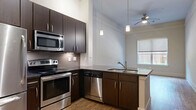 Located at 4100 Greenbriar Dr in Houston's 77098 zip code, this one-bedroom, one-bathroom unit offers a well-designed single-floor layout. The open-concept kitchen, dining, and living area serves as the heart of the home, featuring warm hardwood floors, soaring ceilings, and abundant natural light. The kitchen is equipped with a full suite of stainless steel appliances — including a refrigerator, electric range, microwave, and dishwasher — set against rich dark-espresso cabinetry and a grey tile backsplash. A peninsula with a dark countertop provides additional workspace and casual seating, while pendant lighting and a ceiling fan with light add a polished finish to the space. A pantry and two closets offer practical storage throughout. The bedroom is a comfortable retreat, finished with plush carpet flooring, neutral walls, and a window that frames views of the surrounding greenery, filling the room with natural light. The bathroom features a full soaking tub with a tiled shower surround and tile flooring, maintaining a clean, neutral aesthetic. A hallway connects the living areas to the private spaces, completing this efficient and thoughtfully arranged floor plan.