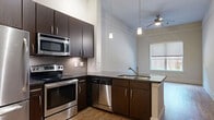 Located at 4100 Greenbriar Dr in Houston's 77098 zip code, this one-bedroom, one-bathroom unit offers a well-designed single-floor layout. The open-concept kitchen, dining, and living area serves as the heart of the home, featuring warm hardwood floors, soaring ceilings, and abundant natural light. The kitchen is equipped with a full suite of stainless steel appliances — including a refrigerator, electric range, microwave, and dishwasher — set against rich dark-espresso cabinetry and a grey tile backsplash. A peninsula with a dark countertop provides additional workspace and casual seating, while pendant lighting and a ceiling fan with light add a polished finish to the space. A pantry and two closets offer practical storage throughout. The bedroom is a comfortable retreat, finished with plush carpet flooring, neutral walls, and a window that frames views of the surrounding greenery, filling the room with natural light. The bathroom features a full soaking tub with a tiled shower surround and tile flooring, maintaining a clean, neutral aesthetic. A hallway connects the living areas to the private spaces, completing this efficient and thoughtfully arranged floor plan.