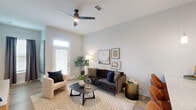 This one-bedroom, one-bathroom unit in Baton Rouge, Louisiana offers a thoughtfully designed open-concept floor plan that maximizes functionality and flow. The kitchen and living area share a seamless, connected space anchored by a large granite-topped island with an undermount sink and bar seating for multiple guests. The kitchen is outfitted with gray shaker-style cabinetry, a white subway tile backsplash, stainless steel appliances including a refrigerator, electric range, and built-in microwave, all complemented by light wood-style flooring throughout. Pendant lighting over the island and soaring ceilings contribute to an open, airy atmosphere. The living area benefits from generous natural light provided by multiple windows and a glass-paneled door, along with a ceiling fan overhead. The bedroom features plush carpet, a ceiling fan, a window with an exterior view, and direct access to a dedicated closet. The bathroom is finished with wood-look flooring, a glass-enclosed shower, and clean neutral tones. Throughout the unit, a consistent palette of soft grays and whites creates a cohesive, modern aesthetic.