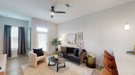 This one-bedroom, one-bathroom unit in Baton Rouge, Louisiana offers a thoughtfully designed open-concept floor plan that maximizes functionality and flow. The kitchen and living area share a seamless, connected space anchored by a large granite-topped island with an undermount sink and bar seating for multiple guests. The kitchen is outfitted with gray shaker-style cabinetry, a white subway tile backsplash, stainless steel appliances including a refrigerator, electric range, and built-in microwave, all complemented by light wood-style flooring throughout. Pendant lighting over the island and soaring ceilings contribute to an open, airy atmosphere. The living area benefits from generous natural light provided by multiple windows and a glass-paneled door, along with a ceiling fan overhead. The bedroom features plush carpet, a ceiling fan, a window with an exterior view, and direct access to a dedicated closet. The bathroom is finished with wood-look flooring, a glass-enclosed shower, and clean neutral tones. Throughout the unit, a consistent palette of soft grays and whites creates a cohesive, modern aesthetic.