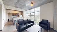 Located at 800 W Marietta St NW in Atlanta's dynamic West Midtown neighborhood, this single-floor unit showcases a distinctive industrial-modern aesthetic throughout. The open-concept living area is anchored by soaring exposed concrete ceilings, polished concrete floors, and a dramatic wall of floor-to-ceiling windows that flood the space with natural light and offer views of the surrounding greenery and cityscape. The living room comfortably accommodates seating and entertainment, with exposed concrete columns adding architectural character.

The kitchen features rich, dark wood cabinetry, granite countertops, and a full suite of stainless steel appliances including a refrigerator, range, and microwave. A granite-topped breakfast bar with bar stool seating connects the kitchen seamlessly to the living area, making it ideal for casual dining and entertaining.

The bedroom is a private, well-defined retreat with a natural light window, built-in desk and shelving, and the same signature exposed concrete detailing found throughout the unit. The hallway provides access to louvered utility and storage doors, along with an electrical panel. The bathroom is clean and functional, featuring a tub/shower combo with white tile surround, dark wood vanity with granite countertop, and polished fixtures throughout.