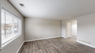 This two-story residence is finished with a consistent, neutral color palette of warm greige tones throughout, creating a clean and cohesive aesthetic. The main living areas feature durable wood-look plank flooring, which extends through the kitchen and main floor spaces, while the bedrooms are finished with plush carpeting for added comfort.

The kitchen is a functional standout, equipped with rich dark-cherry cabinetry offering generous storage, granite-look countertops, a stainless steel sink, and a full suite of black appliances including a refrigerator, electric range, microwave, and dishwasher. A ceiling fan provides ventilation above.

The living and secondary rooms are generously proportioned, each featuring textured ceilings, white baseboards, and windows that introduce natural light. A white-railed staircase connects the two floors, with a closet nearby adding practical storage at the landing area.

The bathroom is cleanly appointed with a tiled tub-shower surround, wood-toned vanity, and wood-look flooring that mirrors the rest of the home. Overall, the space presents a functional and well-maintained interior with a straightforward, modern-neutral design sensibility.
