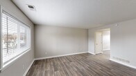 This two-story residence is finished with a consistent, neutral color palette of warm greige tones throughout, creating a clean and cohesive aesthetic. The main living areas feature durable wood-look plank flooring, which extends through the kitchen and main floor spaces, while the bedrooms are finished with plush carpeting for added comfort.

The kitchen is a functional standout, equipped with rich dark-cherry cabinetry offering generous storage, granite-look countertops, a stainless steel sink, and a full suite of black appliances including a refrigerator, electric range, microwave, and dishwasher. A ceiling fan provides ventilation above.

The living and secondary rooms are generously proportioned, each featuring textured ceilings, white baseboards, and windows that introduce natural light. A white-railed staircase connects the two floors, with a closet nearby adding practical storage at the landing area.

The bathroom is cleanly appointed with a tiled tub-shower surround, wood-toned vanity, and wood-look flooring that mirrors the rest of the home. Overall, the space presents a functional and well-maintained interior with a straightforward, modern-neutral design sensibility.
