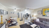 This two-story unit is thoughtfully laid out across two floors, with the main level housing the primary living spaces and the upper level offering a more intimate, private retreat. The main floor features an open-concept design where the living room, dining area, and kitchen flow seamlessly together. The living room is bright and welcoming, with large windows dressed in sheer curtains that allow natural light to fill the space, complemented by crown molding and a ceiling fan overhead. Hardwood-style flooring runs throughout, adding warmth and continuity.

The kitchen is well-appointed with white cabinetry, dark granite countertops, stainless steel appliances including a refrigerator, range, and over-the-range microwave, and a breakfast bar with seating — ideal for casual dining. A separate dining area with a round table sits adjacent to the kitchen.

The bedrooms are comfortably proportioned, each featuring crown molding, hardwood-style floors, and closet space. One bedroom includes a built-in desk area and a walk-in closet. Both bathrooms are clean and functional, featuring light wood-tone flooring, dark countertops, and shower-tub combinations. Two hallways and two staircases connect the floors efficiently, and a dedicated closet provides additional storage.