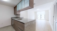 This single-floor residence showcases a clean, contemporary design with a cohesive aesthetic carried throughout the space. The open-concept living and kitchen area forms the heart of the home, where light hardwood flooring extends seamlessly from room to room, creating a warm yet modern atmosphere.

The kitchen is a standout feature, designed with both function and style in mind. It is equipped with stainless steel appliances, including a French door refrigerator with an ice and water dispenser, a range, and an over-the-range microwave. Granite countertops run along both the perimeter cabinetry and a peninsula that separates the kitchen from the living area. Upper cabinetry features frosted glass-panel doors with warm wood-toned frames, adding a refined, contemporary touch. Tile flooring anchors the kitchen zone. Large windows at the far end of the living area flood the space with natural light and offer views of the surrounding building exterior.

The bedroom is bright and airy, featuring the same light hardwood flooring, a wide window fitted with a roller shade, and clean white walls that contribute to an open, uncluttered feel. The bathroom offers a granite-topped vanity with a wood-grain cabinet base, a large mirror, and a glass-enclosed shower, all finished with neutral tile flooring. The overall ambiance of this residence is modern, light-filled, and thoughtfully designed.