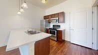 Located at 147 N Harold St in Salt Lake City, Utah, this single-floor residence offers a clean, functional layout designed for comfortable everyday living. The open-concept kitchen serves as the heart of the home, featuring rich dark wood cabinetry, light countertops, a double-basin sink set into a peninsula island, and a full suite of stainless steel appliances including a refrigerator, electric range, over-the-range microwave, and dishwasher. A trio of pendant lights hang above the kitchen peninsula, providing both task lighting and a stylish focal point that connects the kitchen to the adjoining living area. Wood-style plank flooring runs throughout the main living spaces, adding warmth and visual continuity. The bedrooms are carpeted for added comfort and each features large windows with horizontal blinds, allowing generous natural light and views of the surrounding greenery. The clean, neutral wall tones throughout the unit create a bright and inviting ambiance. The bathroom is well-appointed with a vanity featuring matching dark wood cabinetry, a single-basin sink with a large mirror, tile flooring, and a shower-tub combination. A textured ceiling in the kitchen area adds a classic touch to the overall design of this well-maintained, move-in ready home.