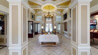 This sophisticated single-story clubhouse exudes classic elegance through its refined architectural detailing and carefully appointed interiors. The grand entrance foyer welcomes visitors with soaring double-height ceilings, ornate wainscoting, decorative pilasters, and a stunning inlaid tile medallion set into the floor beneath floor-to-ceiling draped windows framing French doors.

The expansive main lobby continues the sense of grandeur, featuring a dramatic coffered ceiling with a central medallion detail, a sweeping chandelier, and tall clerestory windows that flood the space with natural light. Comfortable seating arrangements anchored by an ornate coffee table create an inviting gathering area.

A leasing and reception area with rich dark wood millwork and integrated display screens provides a polished, professional environment, with private offices nearby that are appointed with formal furnishings, intricate crown molding, and draped windows.

The entertainment lounge is a standout feature, housing a full-size billiards table, a handsome dark wood bar with mirrored backlit shelving, and a stylishly patterned carpet that ties the space together. Ambient cove lighting adds a warm, club-like atmosphere.

A dedicated business center offers built-in granite-topped workstations with upper cabinetry, providing a functional and polished workspace. Throughout the clubhouse, consistent use of neutral tones, wainscoting, and decorative moldings creates a cohesive and upscale ambiance.