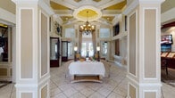 This sophisticated single-story clubhouse exudes classic elegance through its refined architectural detailing and carefully appointed interiors. The grand entrance foyer welcomes visitors with soaring double-height ceilings, ornate wainscoting, decorative pilasters, and a stunning inlaid tile medallion set into the floor beneath floor-to-ceiling draped windows framing French doors.

The expansive main lobby continues the sense of grandeur, featuring a dramatic coffered ceiling with a central medallion detail, a sweeping chandelier, and tall clerestory windows that flood the space with natural light. Comfortable seating arrangements anchored by an ornate coffee table create an inviting gathering area.

A leasing and reception area with rich dark wood millwork and integrated display screens provides a polished, professional environment, with private offices nearby that are appointed with formal furnishings, intricate crown molding, and draped windows.

The entertainment lounge is a standout feature, housing a full-size billiards table, a handsome dark wood bar with mirrored backlit shelving, and a stylishly patterned carpet that ties the space together. Ambient cove lighting adds a warm, club-like atmosphere.

A dedicated business center offers built-in granite-topped workstations with upper cabinetry, providing a functional and polished workspace. Throughout the clubhouse, consistent use of neutral tones, wainscoting, and decorative moldings creates a cohesive and upscale ambiance.