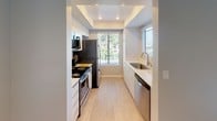 Located in Lake Forest, California, this single-floor residence showcases a clean, modern aesthetic throughout. The open living area immediately impresses with soaring vaulted ceilings that amplify the sense of space, neutral carpeting underfoot, and a ceiling fan that adds a functional touch. A window with blinds invites natural light and views of the surrounding greenery.

The galley-style kitchen is thoughtfully designed with crisp white cabinetry lining both sides, light wood-look flooring, and a tray ceiling with recessed lighting overhead. Stainless steel appliances — including a refrigerator, range, microwave, and dishwasher — complement the clean white countertops. An undermount stainless steel sink is positioned beneath a window overlooking lush outdoor landscaping.

The bedrooms are generously proportioned, each finished with soft neutral carpet and light gray walls. Vaulted ceiling lines continue into the primary bedroom, which opens to an en-suite bathroom and walk-in closet. The bathroom features a long floating white vanity with dual sinks, a large mirror, and mirrored sliding closet doors, all finished in a bright, minimalist style with wood-look tile flooring.

Throughout the home, the consistent use of light tones, natural light, and modern finishes creates a cohesive, contemporary ambiance well-suited to comfortable everyday living in Southern California.