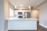 Located at 150 Greenbrier Rd in Cambridge, Ontario, this well-appointed two-bedroom, two-bathroom unit offers a thoughtfully designed single-floor layout with modern finishes throughout. Warm hardwood-style flooring flows seamlessly across the entire space, complemented by neutral grey tones and crisp white trim that lend a clean, contemporary feel.

The open-concept kitchen and living area serves as the heart of the home. The kitchen is equipped with stainless steel appliances — including a refrigerator, range, and over-the-range microwave — alongside sleek white cabinetry, a white quartz countertop, and a peninsula with an undermount double sink. Pendant lighting and a large window fill the space with natural light and views of the surrounding neighbourhood.

The spacious living area features large windows that overlook the cityscape, providing ample natural light. Both bedrooms are generously proportioned, with the primary bedroom offering a comfortable footprint, large windows with neighbourhood views, and access to a closet. In-suite stacked washer and dryer laundry is conveniently located within the unit.

The two bathrooms are finished in clean white, one featuring a full soaker tub with shower combination and the other a stand-alone shower stall. A well-lit hallway connects all rooms efficiently, completing this practical and modern living space.