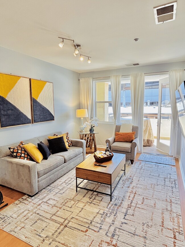 Espacio de estar abierto y luminoso con televisor inteligente 4K de 65", sofá cama y luz natural. - 3687 4th Ave