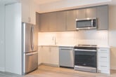 Located at 41 Johnson Street in Barrie, Ontario, this thoughtfully designed one-bedroom, one-bathroom unit offers a modern and efficient single-floor layout. Light-toned luxury vinyl plank flooring flows throughout, unifying the open-concept living, dining, and kitchen areas and creating a bright, cohesive atmosphere.

The kitchen is a standout feature, outfitted with two-tone cabinetry in white and grey, a classic subway tile backsplash, light quartz countertops, and a full suite of stainless steel appliances including a refrigerator, electric range, built-in microwave, and dishwasher. Track lighting overhead ensures excellent task illumination.

The combined living and dining area is bathed in natural light from large floor-to-ceiling windows, offering views of the surrounding Barrie streetscape. The bedroom is a comfortable, well-proportioned retreat featuring a sliding double-panel closet and a sliding glass door that opens onto a private balcony with modern glass railing.

The bathroom is finished with neutral large-format floor tiles and textured wall tiles surrounding a full soaker tub with an adjustable showerhead. A white vanity with under-cabinet storage and a large mirror completes the space. A stacked in-unit washer and dryer are conveniently located adjacent to the bathroom. The hallway connects all rooms efficiently, maximizing the use of the available footprint.