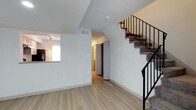 This two-floor residence offers a straightforward and functional layout designed for comfortable everyday living. The main level features light-toned hardwood flooring that extends throughout the open living area, creating a bright and cohesive feel. The textured ceilings add a subtle architectural detail, while large white walls provide a clean, neutral backdrop throughout the space. A notable feature of the main level is the pass-through window connecting the kitchen to the living area, allowing for an open sightline and easy interaction between the two spaces. The kitchen is equipped with a countertop that extends to the pass-through, and track lighting above adds focused illumination. A carpeted staircase with a sleek black metal railing leads to the upper floor, serving as a visual focal point in the main living area. The lower level also includes a hallway leading to additional rooms, with warm wood-toned doors adding contrast to the white walls. Ample storage is accessible off the hallway, contributing to the home's practical design. The overall ambiance is clean, minimal, and move-in ready, with a neutral palette that offers versatility for personalization across both floors.