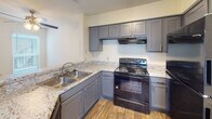 Located at 1300 Longcreek Dr in Columbia, SC, this single-floor residence offers a well-designed layout with comfortable living spaces throughout. The kitchen is a standout feature, equipped with gray shaker-style cabinetry, granite-look countertops, a stainless steel double-basin sink, and black appliances including an electric range. Wood-look flooring and a textured ceiling complete the kitchen's functional yet stylish aesthetic. The living area is bright and open, benefiting from vaulted ceilings, recessed lighting, and a sliding glass door that fills the room with natural light and provides outdoor access. A peninsula counter connects the kitchen to the living space, creating a seamless flow. The bedrooms are generously sized, each featuring plush wall-to-wall carpeting, multiple windows with blinds for natural light and privacy, and ceiling fans with light fixtures. One bedroom showcases impressively tall ceilings, adding a sense of openness. The bathroom is cleanly appointed with a tiled tub-shower combination, a granite-topped vanity with a gray cabinet base, and wood-look flooring that ties back to the kitchen. Overall, the residence presents a cohesive, move-in-ready interior with consistent finishes and ample natural light throughout.