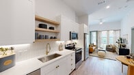 Located at 2022 N Beckley Ave in Dallas, TX, this one-bedroom, one-bathroom residence offers a thoughtfully designed single-floor layout that maximizes every square foot. The open-concept kitchen is a standout feature, showcasing white shaker cabinetry with brushed gold hardware, quartz countertops, a subway tile backsplash, open natural wood shelving, and a full suite of stainless steel appliances. Light wood-look flooring flows seamlessly from the kitchen into the dining and living areas, creating a cohesive and airy feel. The living room benefits from soaring ceilings, a large sliding glass door that invites natural light and outdoor views, and a ceiling fan overhead. A hallway connects the main living spaces to the private bedroom, which features plush carpet flooring, tall ceilings, large windows with outdoor views, and access to a dedicated closet with built-in shelving. The bathroom is finished with a white vanity with gold fixtures, a framed mirror, and a glass-enclosed walk-in shower. A convenient hallway with additional storage rounds out this well-planned residence, offering a clean, modern aesthetic with warm design accents throughout.