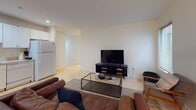 This single-floor residence offers a thoughtfully organized layout that balances comfort and functionality across its key living spaces. Light hardwood flooring runs throughout, providing a warm, cohesive foundation that ties the rooms together seamlessly.

The living area is bright and welcoming, featuring two windows fitted with horizontal blinds that allow for adjustable natural light. It is furnished with rich brown leather seating, a glass-top coffee table, a large flat-screen television on a media console, and a cozy accent chair — creating an inviting space for relaxation.

The kitchen is efficiently designed with a full run of white shaker-style cabinetry, ample counter space, a stainless steel sink, and white appliances including a range, over-the-range microwave, dishwasher, and full-size refrigerator. A teal accent wall adds a distinctive pop of color.

Both bedrooms are comfortably sized with neutral cream walls, hardwood floors, and windows with blinds. The primary bedroom includes a wood-framed bed, decorative framed artwork, and direct sightlines to the kitchen. A walk-in closet provides generous storage. The second bedroom features a dark wood dresser and additional framed wall art.

The bathroom is clean and functional, finished with tile flooring, a white vanity with under-cabinet storage, a mirrored medicine cabinet, and a tub-shower combination.