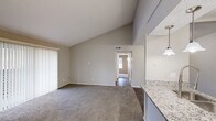 Located at 601 W Renner Rd in Richardson, TX, this two-bedroom, one-bathroom residence offers a well-organized single-story layout with a cohesive, neutral color palette throughout. The combined kitchen and living area serves as the heart of the home, where striking vaulted ceilings lend an open, airy feel to the living space, which features plush carpeting and a view down the hallway connecting the rest of the unit. The kitchen is efficiently designed with dark wood-tone flooring, white cabinetry, granite countertops, and stainless steel appliances including a refrigerator and gas range. Two hallways provide smooth connectivity between living and private areas. The primary bedroom is generously sized and includes a walk-in closet, while the second bedroom also features its own closet and a window with natural light. Both bedrooms are finished with soft carpet. The bathroom is well-appointed with a granite-topped vanity, white cabinetry, a full soaking tub with shower, and wood-tone flooring that ties cohesively to the kitchen. Ceiling fans are present in the bedrooms for added comfort. The overall design emphasizes practicality and clean, modern finishes in a compact and efficient floor plan.