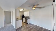 This single-floor residence offers a practical and comfortable layout designed for everyday living. The living area is generously sized, featuring plush carpet flooring, neutral gray walls, and a large front-facing window that fills the space with natural light and views of the surrounding greenery. A ceiling fan overhead adds both comfort and airflow to the open area. The living space flows seamlessly into the dining and kitchen zone, where durable wood-look flooring transitions underfoot. The kitchen is well-equipped with white cabinetry, dark granite-style countertops, and a full suite of appliances including a black refrigerator, electric range, stainless steel dishwasher, and a sink with ample counter space. A pass-through peninsula connects the kitchen to the dining area, enhancing the open feel. The bedrooms are carpeted and spacious, each featuring neutral tones and access to natural light through well-placed windows. One bedroom provides direct access to a bathroom, offering added convenience. The bathrooms are clean and functional, finished with wood-look flooring, white tiled tub-shower combinations, and updated fixtures. A textured ceiling is present throughout, lending a consistent finish to the entire space.