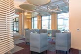 This thoughtfully designed single-floor amenity space in Union, NJ offers a sophisticated blend of collaborative and private areas suited for work, relaxation, and social interaction. The open layout is anchored by a striking wood slat partition wall that serves as a dramatic architectural focal point, dividing zones while maintaining a sense of visual continuity throughout the space.

The lounge area features an eclectic mix of seating, including high-back upholstered chairs, patterned accent seating, and sleek side tables, all arranged beneath eye-catching circular pendant lighting fixtures. Large floor-to-ceiling windows flood this section with natural light and provide views of the surrounding streetscape, enhancing the open, airy ambiance.

A dedicated work zone includes a built-in countertop with bar-height seating set against a textured mosaic tile accent wall, providing a focused workspace alongside a wall-mounted display screen. Nearby, semi-private study nooks with tall divider walls and overhead pendant lighting offer individual workstations for quiet productivity.

Throughout the space, patterned carpet tiles in layered geometric designs add visual depth and help define distinct functional zones. The warm neutral color palette, complemented by natural wood tones and modern fixtures, creates a polished yet welcoming atmosphere.