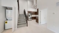 Located at 18300 SW 98th Ave in Palmetto Bay, FL, this modern two-story unit showcases a clean, contemporary design throughout. The main level opens to a bright living area distinguished by soaring double-height ceilings and floor-to-ceiling windows dressed with sleek roller shades, flooding the space with natural light and offering views of the lush landscaping outside. The kitchen is a standout feature, outfitted with rich wood cabinetry, white quartz countertops, a stainless steel refrigerator, and a statement range hood — all framed by a dramatic open volume above. A striking staircase with concrete treads and black metal railings connects the two floors with architectural flair. The upper level hosts generously sized bedrooms, each benefiting from large windows and abundant natural light. A spacious walk-in closet with built-in shelving and dual hanging rods provides excellent storage. The bathrooms are finished to a high standard, featuring wood-toned floating vanities with white countertops and undermount sinks; one bathroom includes a full soaking tub and shower combo, while another offers a glass-enclosed walk-in shower. Light-toned flooring flows consistently throughout, reinforcing the space's bright, minimalist aesthetic.