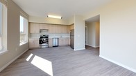 This single-floor unit features a contemporary design with a neutral warm-beige palette and durable grey wood-plank flooring throughout the main living areas. The open-concept living and kitchen space is well-lit, benefiting from multiple large windows and a glass-paneled door that opens to a private balcony overlooking a lush, tree-lined setting. The kitchen is outfitted with light wood laminate cabinetry extending to the upper walls, white quartz countertops, stainless steel appliances including a refrigerator, range, and dishwasher, and an under-mount sink. The layout flows openly between the kitchen and living area, providing a functional and spacious feel.

The bedrooms are carpeted and finished in the same warm-neutral tones, each featuring windows that allow abundant natural light and views of the surrounding neighborhood and greenery. The rooms offer generous proportions suitable for various furniture configurations.

Two full bathrooms serve the unit. One features a dark-countered vanity with wood-grain cabinetry, a large mirror, and a tub-shower combination. The second bathroom is finished in crisp white with light tile flooring and a full tub-shower surround, providing a clean and functional space. Overall, the unit presents a bright, move-in ready environment with modern finishes throughout.