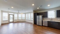 Located at 1700 W Frankford Rd in Carrollton, TX, this single-floor residence offers a thoughtfully designed layout that balances modern aesthetics with everyday functionality. The open-concept living and dining area is a standout feature, showcasing rich hardwood-style flooring, recessed lighting, and a ceiling fan. A generous arrangement of windows — including a sweeping bay-style window bank — floods the space with natural light while offering views of the surrounding area. A glass door provides direct access to a private balcony or outdoor space.

The kitchen is well-appointed with dark espresso cabinetry, light countertops, a white subway tile backsplash, and a full suite of stainless steel appliances including a refrigerator, range, microwave, and dishwasher. The space flows seamlessly into the living area, making it ideal for both cooking and entertaining.

Bedrooms are carpeted for comfort and include ceiling fans and windows that bring in additional natural light. A hallway lined with paneled doors provides access to closets and additional rooms, adding practical storage to the layout.

The bathroom features wood-style flooring, a tub-shower combination with clean white tile surround, dark vanity cabinetry, and light countertops — completing the home's cohesive modern design palette.