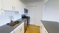 Unit 109G is a thoughtfully laid-out studio with one bathroom, offering an efficient and functional living space on a single floor. The kitchen is a standout feature, designed in a galley style with clean white cabinetry, sleek gray countertops, and a full suite of stainless steel appliances including a gas range, built-in microwave, dishwasher, and sink. Light wood-tone flooring runs throughout, adding warmth and continuity to the space. The white cabinetry is accented with modern bar-pull hardware, contributing to a contemporary aesthetic that feels both fresh and practical. The kitchen layout maximizes counter and storage space on both sides, making meal preparation convenient. The overall design of the unit emphasizes clean lines and a neutral color palette, creating a bright and cohesive atmosphere. The open studio configuration allows for flexible furniture arrangements, making it easy to define distinct living and sleeping areas. This unit is well-suited for individuals seeking a modern, low-maintenance living space with functional amenities in a compact, efficient footprint.