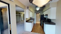 This single-floor, one-bedroom, one-bathroom unit offers a practical and straightforward layout designed for comfortable everyday living. The kitchen is equipped with black appliances, including a refrigerator, electric range with overhead ventilation, and a double-basin sink. White cabinetry provides ample upper and lower storage, complemented by dark countertops. Wood-look flooring runs throughout the kitchen, transitioning to carpet in the adjacent living and bedroom areas.

The living room is a generously sized, carpeted space featuring a corner fireplace framed by built-in display shelving above. A sliding glass door provides access to an outdoor area and allows natural light into the room. The bedroom includes multiple windows on two walls, bringing in additional natural light and views of surrounding greenery, with soft carpet underfoot and a textured ceiling overhead.

The bathroom includes a full tub and shower combination with tiled surround and a curved shower rod. A dedicated utility area houses a water heater and washer, offering added convenience with in-unit laundry capability. Throughout, the unit maintains a neutral color palette with warm beige tones.