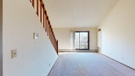 This two-story residence offers a well-organized layout across two floors, with the main level providing generous living space and the upper level hosting the private quarters. The main floor welcomes you through a wood entry door into a carpeted living area filled with natural light from a large sliding glass door. A staircase with classic wood railings rises prominently from the living area, connecting to an open upper-level landing with a view below. The kitchen features warm wood cabinetry and is conveniently accessible from the main living space. The upper floor houses the generously sized primary bedroom, which boasts vaulted ceilings, a large window with outdoor views, and its own dedicated bathroom. Additional bedrooms are well-proportioned, each with carpeted floors, closets featuring sliding wood doors and built-in shelving, and access to shared bathrooms. All three bathrooms are fitted with vanities featuring wood cabinetry, single-basin sinks, and tile flooring. Each bedroom includes a closet, and a large walk-in style closet with built-in wood shelving and a hanging rod offers ample storage. Textured ceilings and baseboard heating are consistent throughout, and ceiling fans provide additional comfort on both levels.
